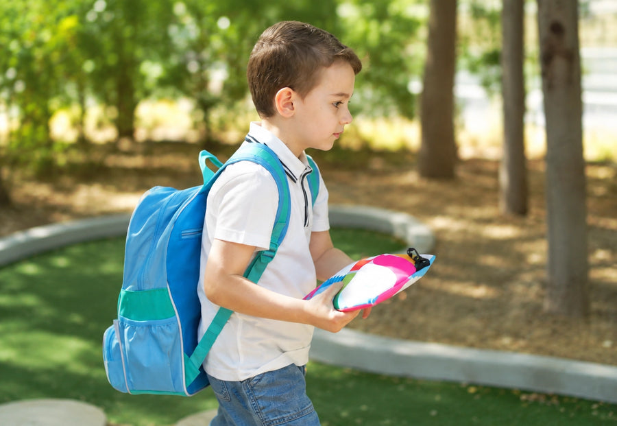 A boy walking outdoors with his backpack, carrying the Moor School Kit